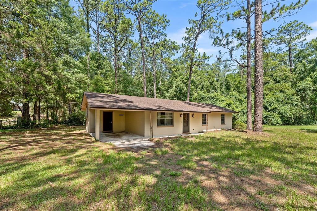 A single-story house with a carport and tan siding sits in a wooded, grassy yard — 22897 COUNTY ROAD 137, LAKE CITY, FL