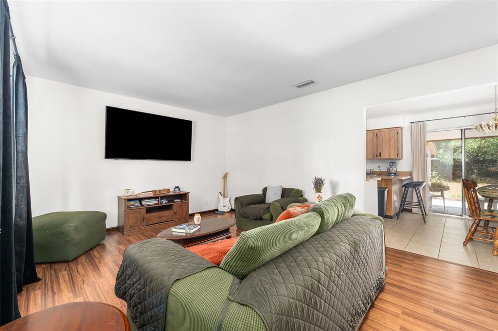 A living room with wood-look flooring, a wall-mounted television, and an adjacent kitchen area — 22897 COUNTY ROAD 137, LAKE CITY, FL