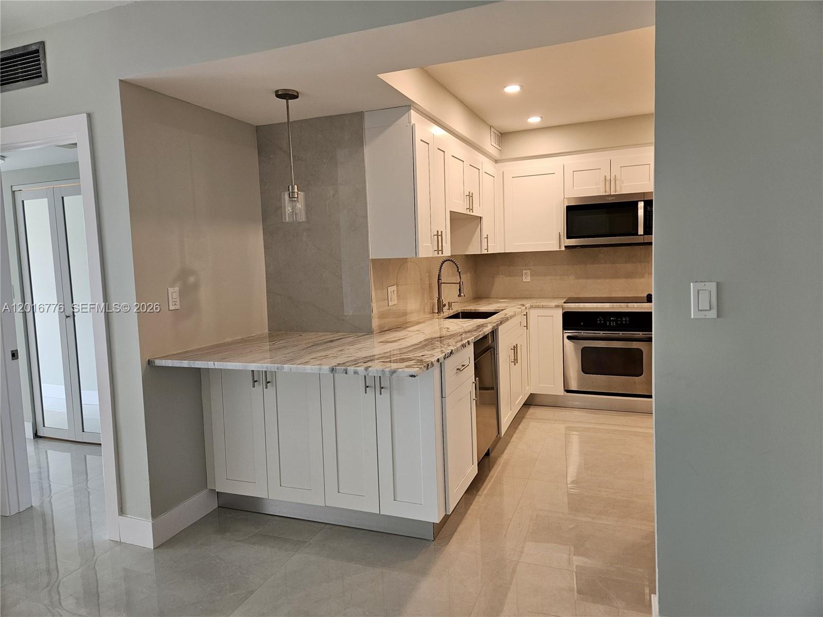 A modern kitchen features white cabinetry, marble countertops, stainless steel appliances, and tile flooring — 1985 S Ocean Dr # 2K, Hallandale Beach FL 33009, HALLANDALE BEACH, FL