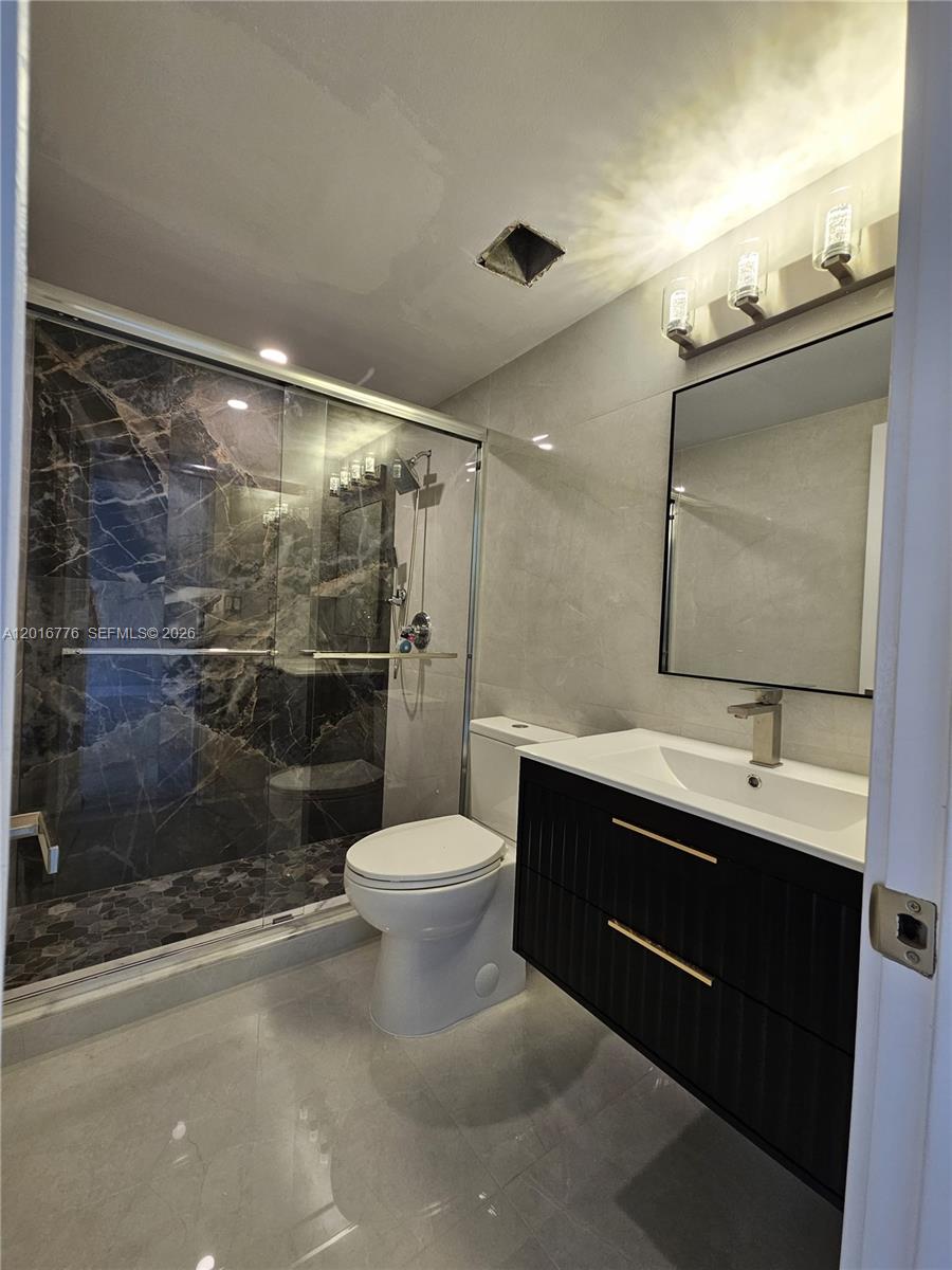 A modern bathroom features a black vanity, a glass-enclosed shower, and gray tile flooring — 1985 S Ocean Dr # 2K, Hallandale Beach FL 33009, HALLANDALE BEACH, FL