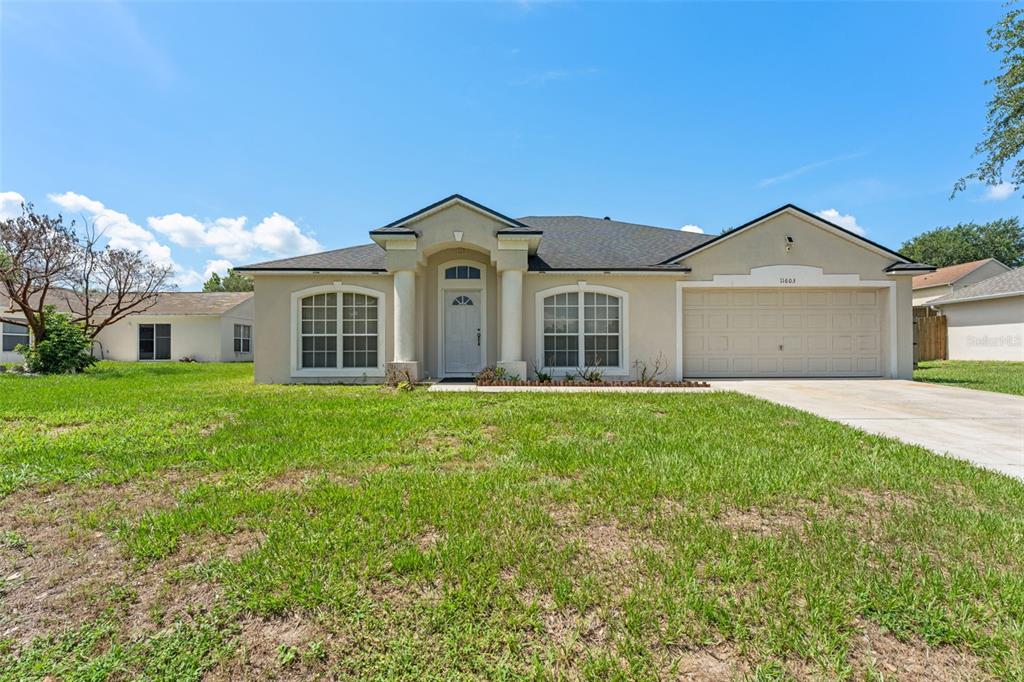 A single-story suburban house with a beige stucco exterior, a two-car garage, and a lawn — 11603 PINELOCH LOOP, CLERMONT, FL