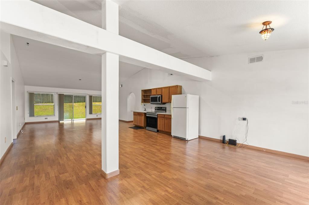 An open-concept living area features wood-look flooring, a kitchen with wood cabinets, and vaulted ceilings — 11603 PINELOCH LOOP, CLERMONT, FL