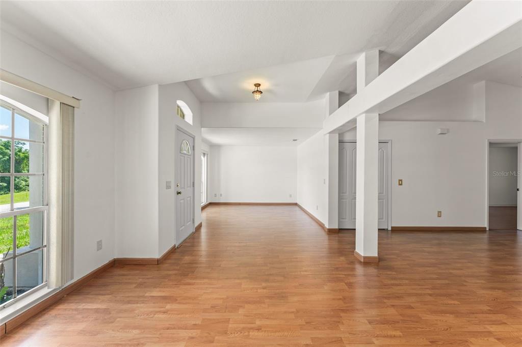 An empty room with wood-look flooring, white walls, a vaulted ceiling, and a support pillar — 11603 PINELOCH LOOP, CLERMONT, FL