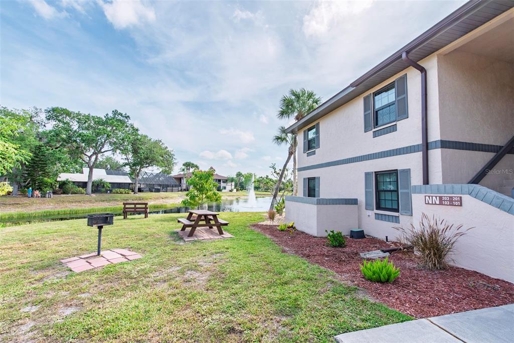 An exterior view of a two-story apartment building with a pond and picnic area — 19505 QUESADA AVENUE UNIT NN101, PORT CHARLOTTE, FL