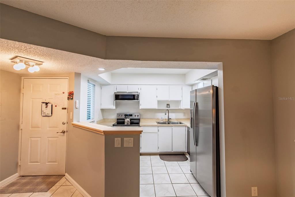 A kitchen with white cabinets and stainless steel appliances opens to an entryway — 19505 QUESADA AVENUE UNIT NN101, PORT CHARLOTTE, FL