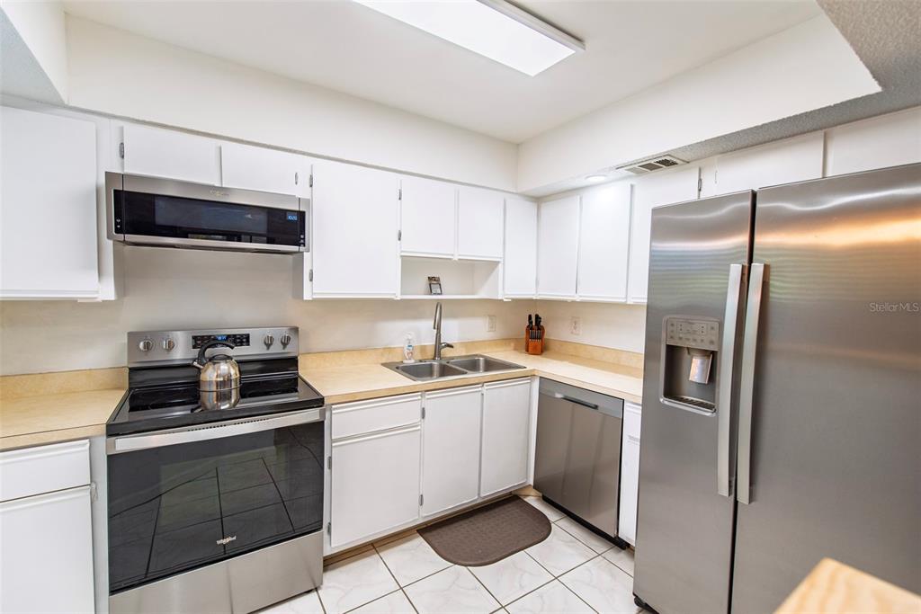 A kitchen features white cabinets, stainless steel appliances, a double sink, and tiled flooring — 19505 QUESADA AVENUE UNIT NN101, PORT CHARLOTTE, FL
