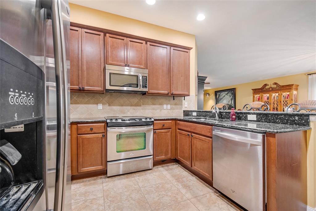 A kitchen features wood cabinets, stainless steel appliances, dark granite countertops, and tile flooring — 11951 FIORE DRIVE, ORLANDO, FL