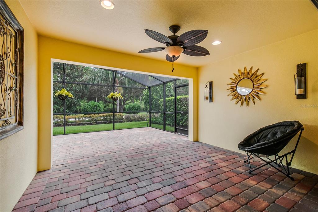 A covered patio with brick pavers, a ceiling fan, and a screened-in view of greenery — 11951 FIORE DRIVE, ORLANDO, FL