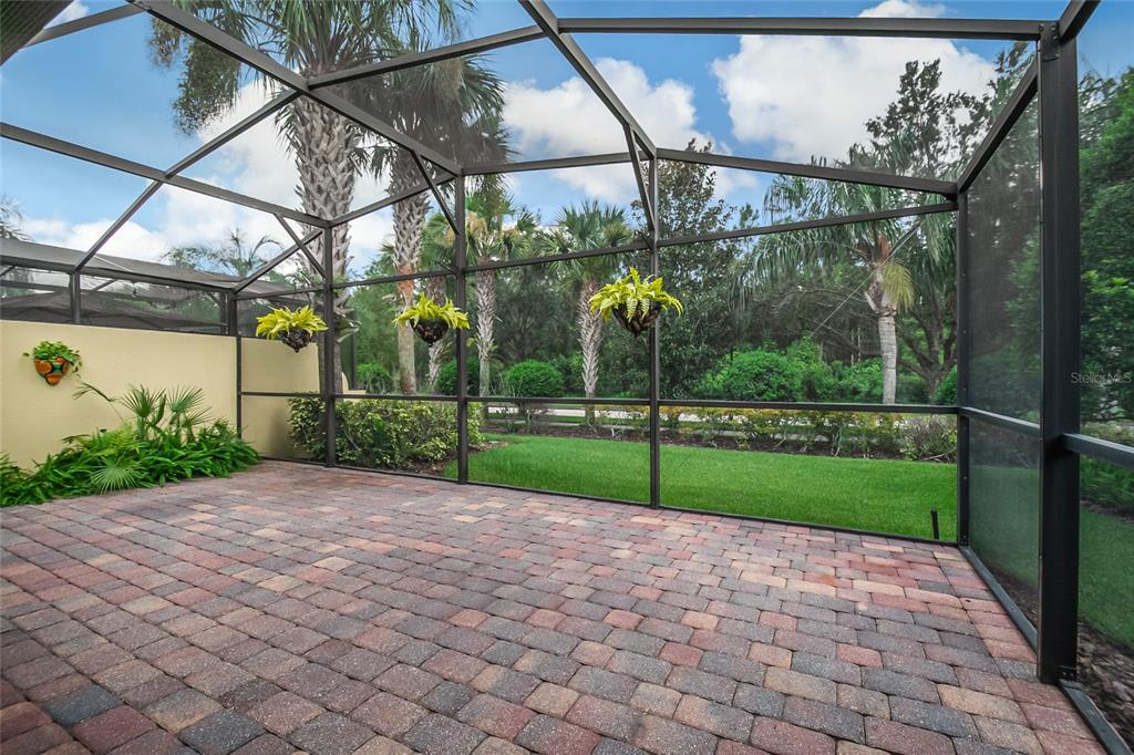 A screened-in patio features brick pavers, hanging plants, and a view of the backyard — 11951 FIORE DRIVE, ORLANDO, FL