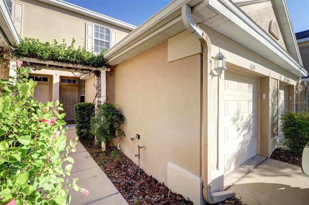 A beige stucco townhouse exterior features a white garage door, a covered entryway, and landscaping — 6243 DUCK KEY COURT, TAMPA, FL