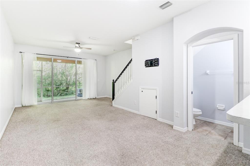 A carpeted living room features a staircase, a small storage door, and a sliding glass door — 6243 DUCK KEY COURT, TAMPA, FL