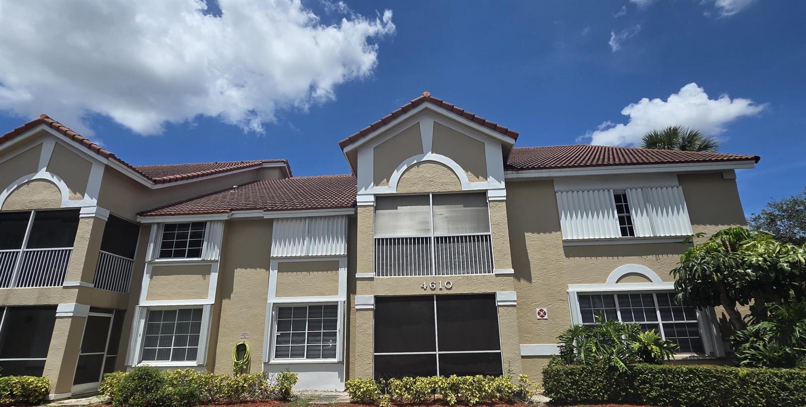 The exterior of a two-story tan stucco building features a tiled roof and screened balconies — 4610 W Mcnab Road # D1, Pompano Beach FL 33069, POMPANO BEACH, FL
