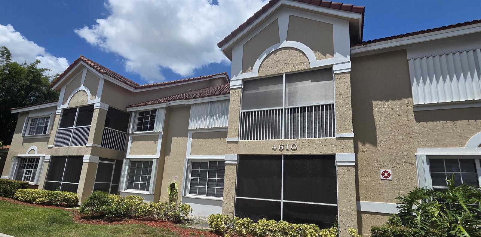 A two-story tan apartment building features screened balconies, white trim, and a tiled roof — 4610 W Mcnab Road # D1, Pompano Beach FL 33069, POMPANO BEACH, FL