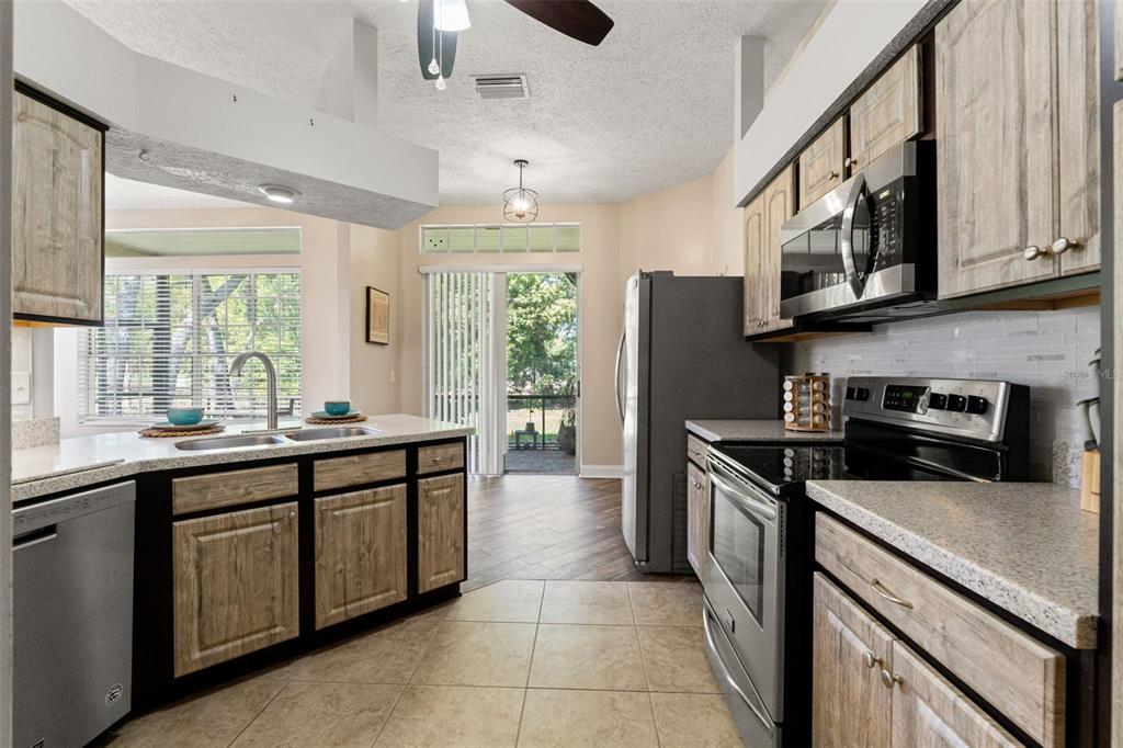 A kitchen features wood-toned cabinets, stainless steel appliances, tile flooring, and a sliding glass door — 10311 PINENEEDLES DRIVE, NEW PORT RICHEY, FL