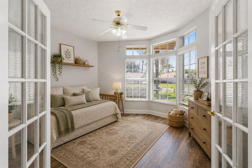 A bedroom with a daybed, wood-look flooring, a ceiling fan, and large bay windows — 10311 PINENEEDLES DRIVE, NEW PORT RICHEY, FL