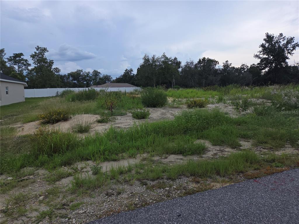 A vacant, grassy lot with sandy patches sits next to a house and white fence — Lot 32 SPRUCE PASS, OCALA, FL