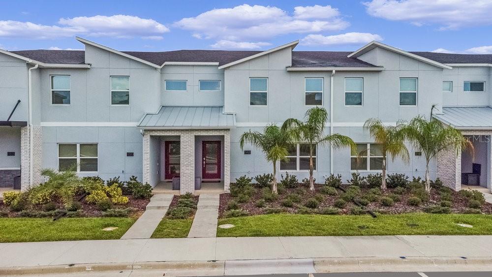 A row of modern two-story townhouses with light blue siding, red front doors, and palm trees — 1148 KINGSBARN STREET, DAVENPORT, FL