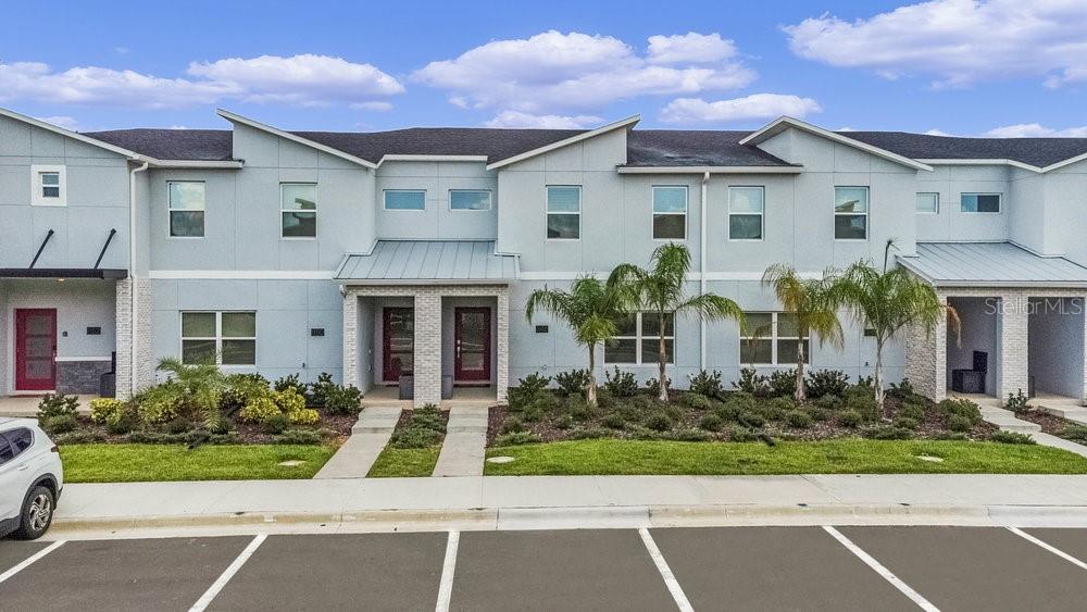 A row of modern, light-blue townhouses with metal roof accents and landscaped front yards — 1148 KINGSBARN STREET, DAVENPORT, FL