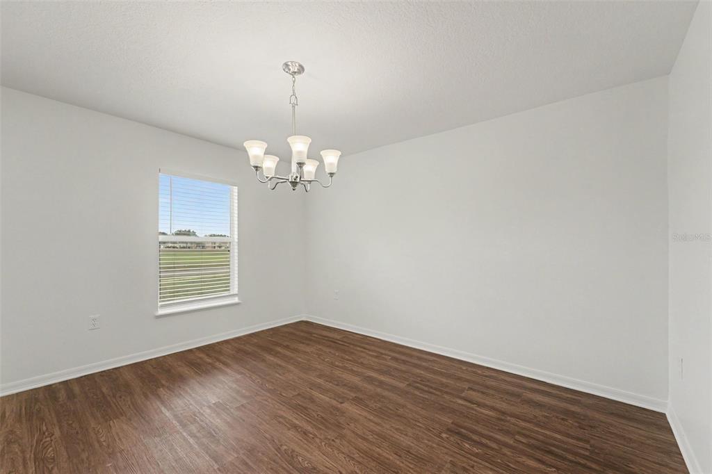 An empty dining room features wood-look flooring, white walls, and a hanging chandelier — 2007 ELMHURST LANE, MASCOTTE, FL
