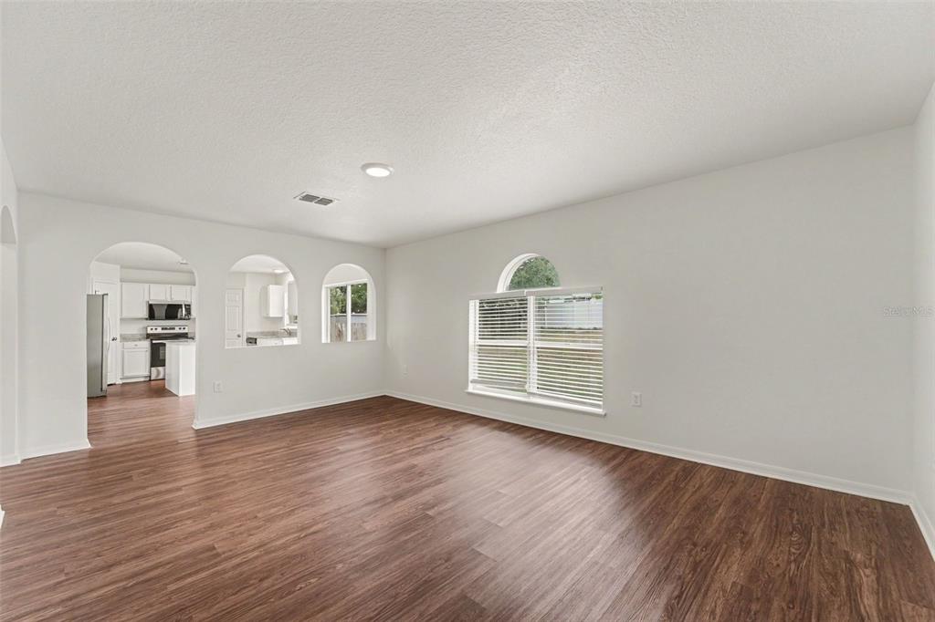 An empty living room with wood-look flooring, white walls, and an arched window — 2007 ELMHURST LANE, MASCOTTE, FL