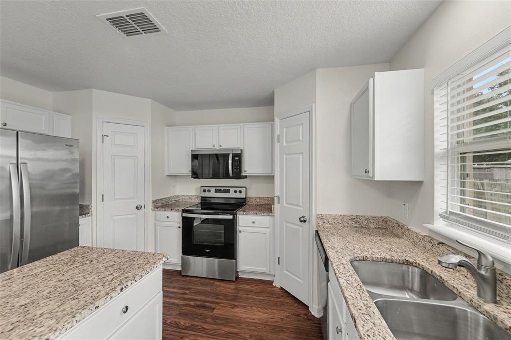 A kitchen features white cabinets, granite countertops, stainless steel appliances, and wood-look flooring — 2007 ELMHURST LANE, MASCOTTE, FL