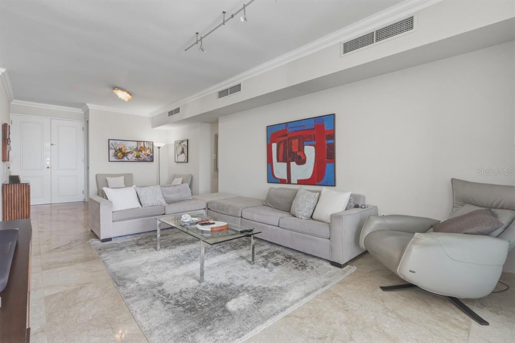 A living room features light tile floors, a gray sectional sofa, and abstract wall art — Cond. Puerto Paseos AVENIDA FELISA RINCON GAUTIER UNIT 2104, SAN JUAN, PR