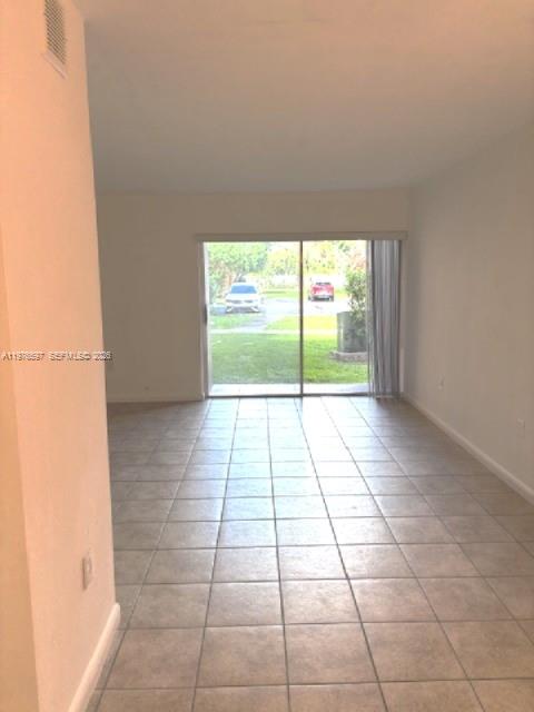 An empty room with light-colored tile flooring and a sliding glass door leading outside — 9493 SW 76th St # L4, Miami FL 33173, MIAMI, FL