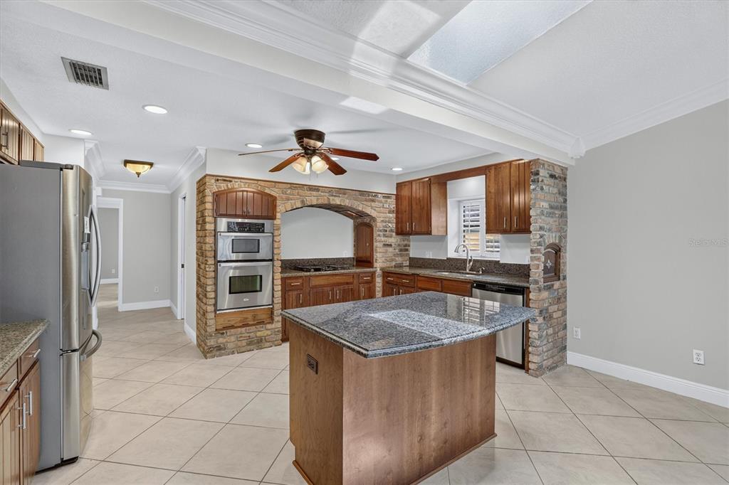 A kitchen features a granite-topped island, stainless steel appliances, and a brick-accented arched wall — 306 OAK ESTATES DRIVE, ORLANDO, FL