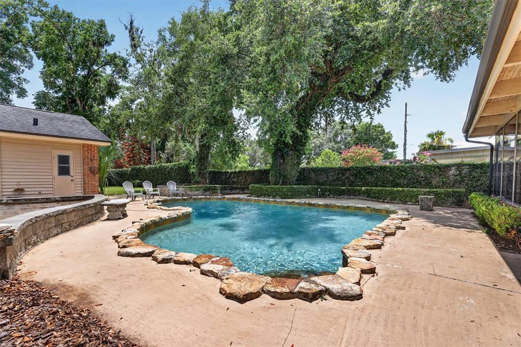 A backyard features a freeform swimming pool with a stone border and a detached garage — 306 OAK ESTATES DRIVE, ORLANDO, FL