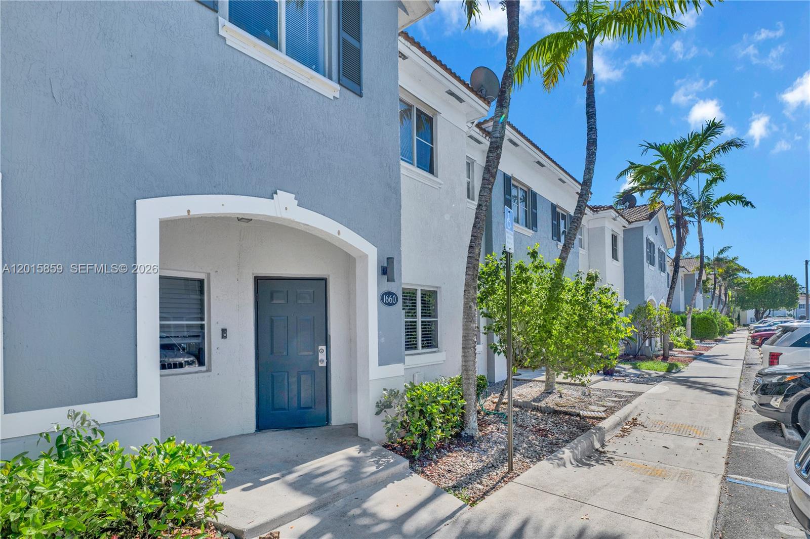 A blue two-story townhouse exterior features a covered entryway, a dark door, and palm trees — 1660 SE 30th St, Homestead FL 33035, HOMESTEAD, FL