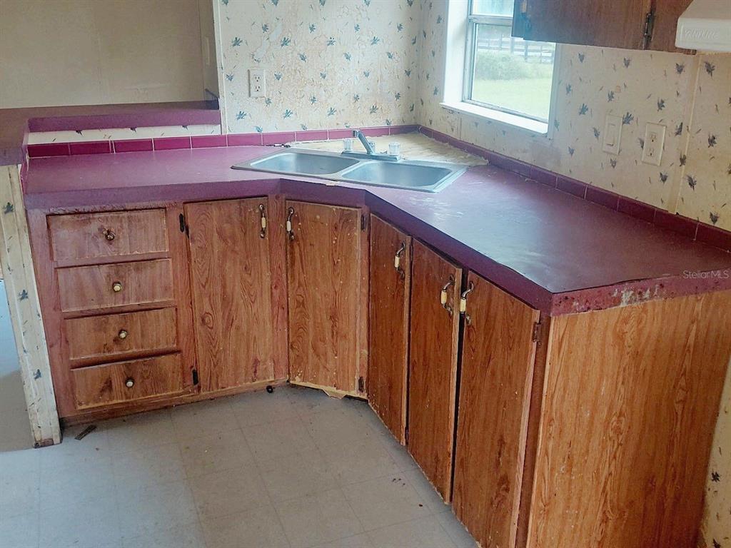 A kitchen features wood cabinets, a purple countertop, a double sink, and floral wallpaper — 1289 SW BEDENBAUGH LANE, LAKE CITY, FL