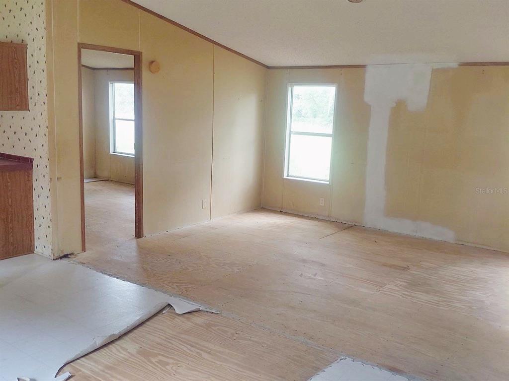 An interior view of a room with unfinished plywood flooring and beige paneled walls — 1289 SW BEDENBAUGH LANE, LAKE CITY, FL