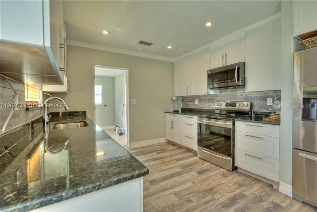 A kitchen features white cabinets, dark granite countertops, stainless steel appliances, and wood-look flooring — 5321 3 RD AVE W, Bradenton FL 34209, BRADENTON, FL
