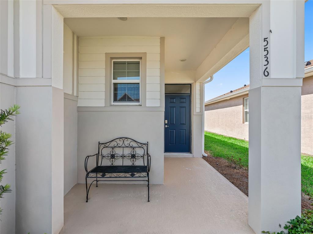 A covered front porch features a black metal bench and a dark blue front door — 5536 NW 40TH LOOP, OCALA, FL