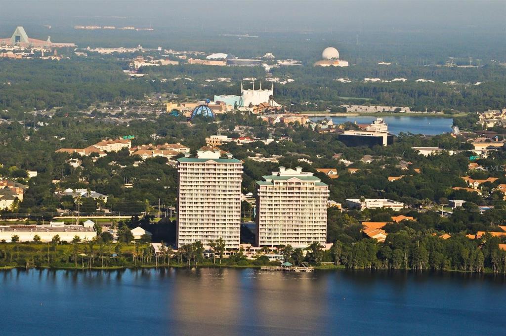 An aerial view shows two high-rise buildings situated on a lake near theme park landmarks — 13427 BLUE HERON BEACH DRIVE UNIT 2107, ORLANDO, FL