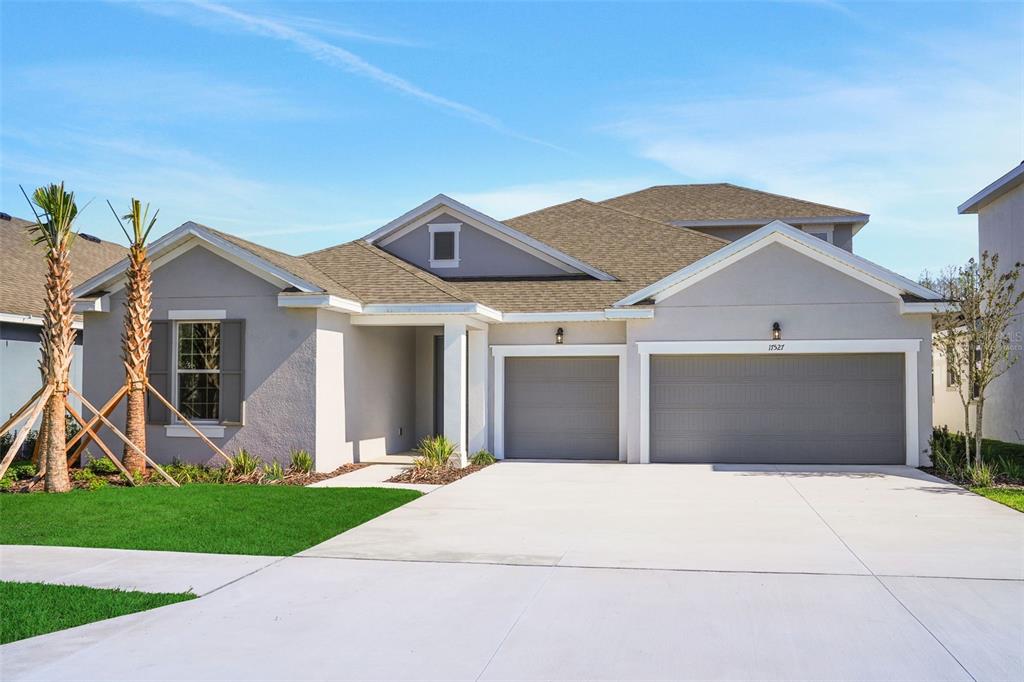 A single-story suburban house with a three-car garage, light gray stucco, and a shingled roof — 17527 VALLEYWOOD PARKWAY, LAND O LAKES, FL