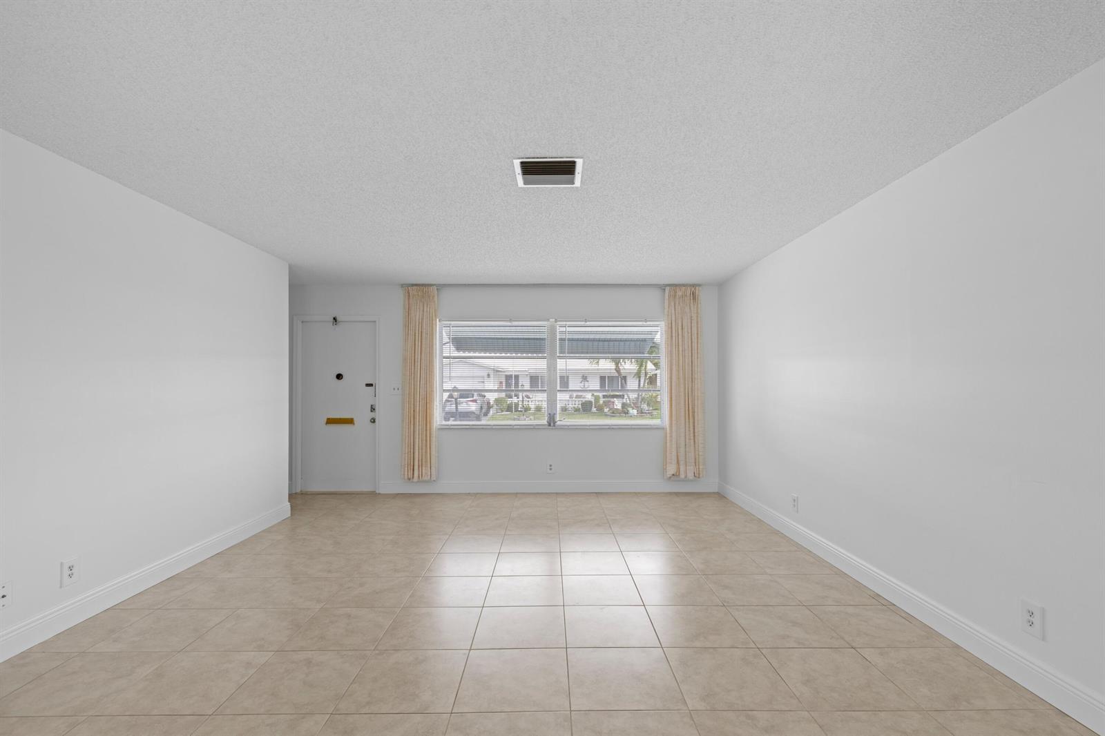 An empty room features white walls, beige tile flooring, a window with curtains, and a door — 1714 SW 19th Drive, Boynton Beach FL 33426, BOYNTON BEACH, FL