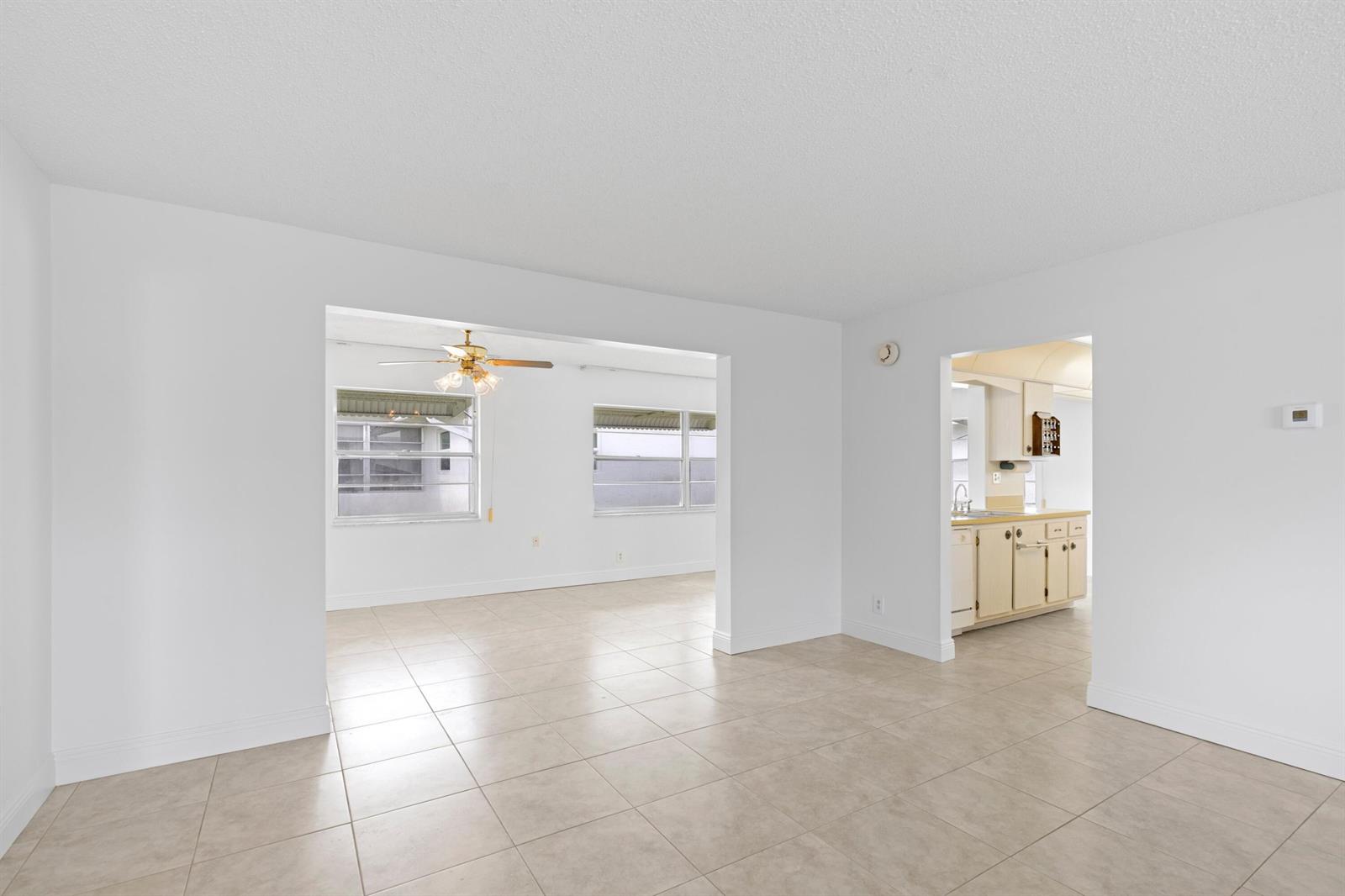 A bright, empty living area with white walls, tile flooring, and an adjacent kitchen — 1714 SW 19th Drive, Boynton Beach FL 33426, BOYNTON BEACH, FL