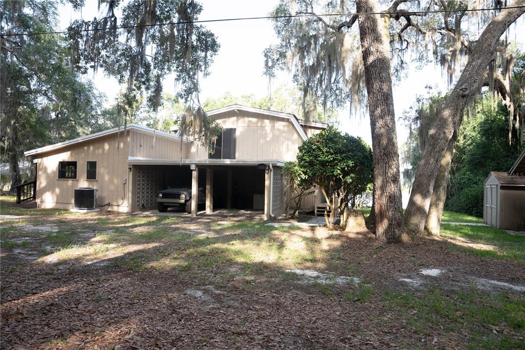 A two-story house with a carport and tan siding sits among trees with Spanish moss — 122 COWPEN LANE, HAWTHORNE, FL