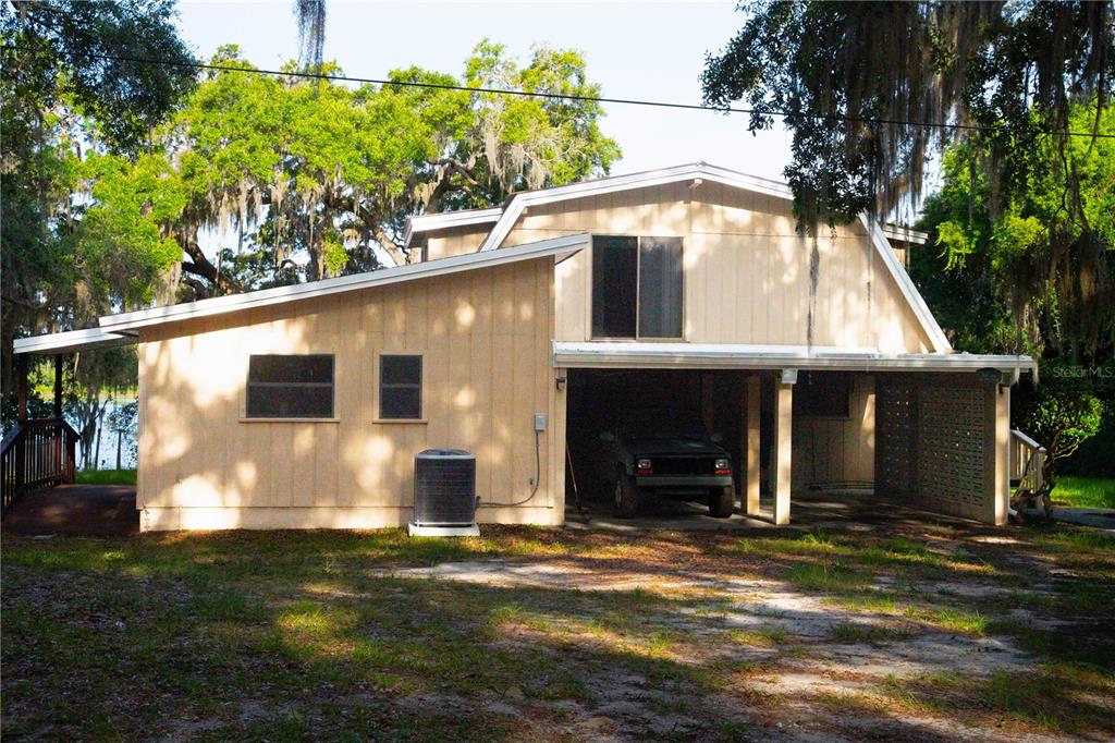 A two-story house with light-colored vertical siding features a carport and a large shade tree — 122 COWPEN LANE, HAWTHORNE, FL