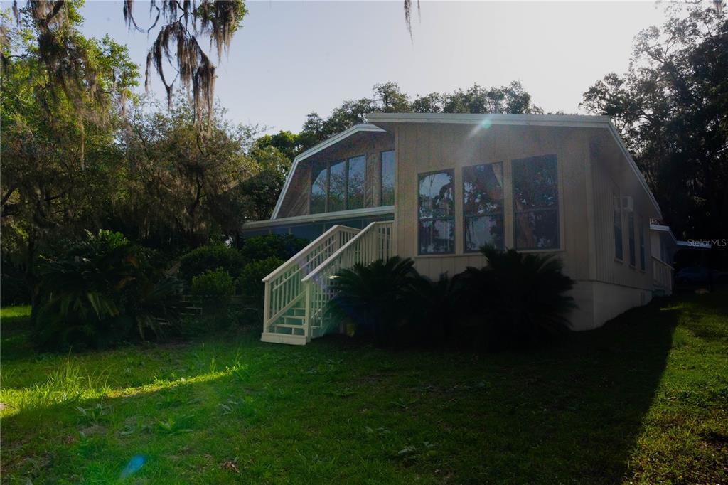 A tan house with a gambrel roof and a white staircase leading to a deck — 122 COWPEN LANE, HAWTHORNE, FL