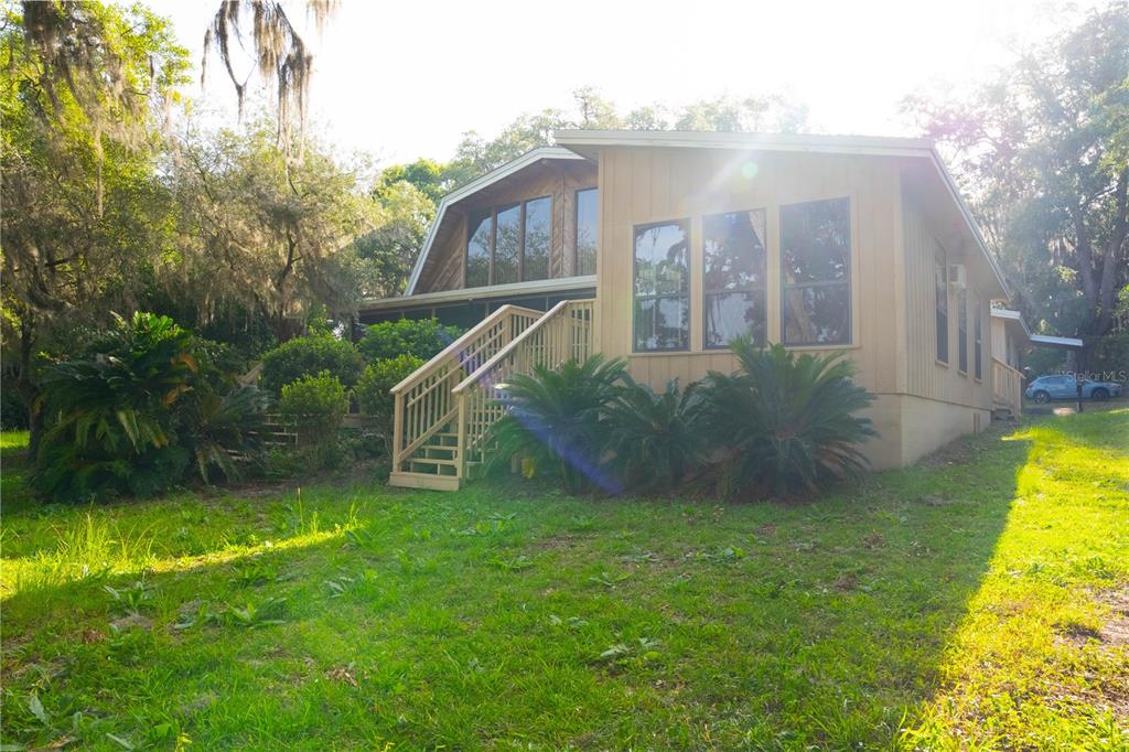 An exterior view of a tan house with large windows, a wooden deck, and stairs — 122 COWPEN LANE, HAWTHORNE, FL