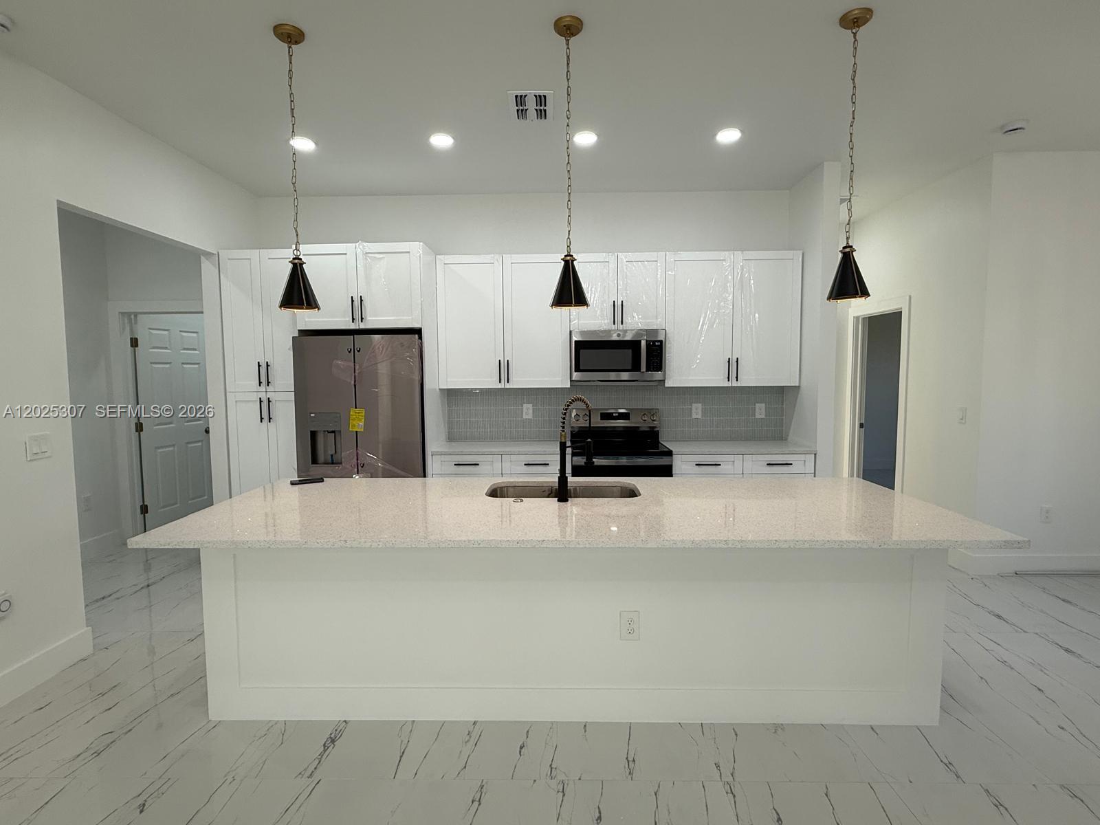 A modern kitchen features white cabinets, a large quartz-topped island, and black pendant lights — 4007 E 13 ST, Lehigh Acres FL 33972, LEHIGH ACRES, FL