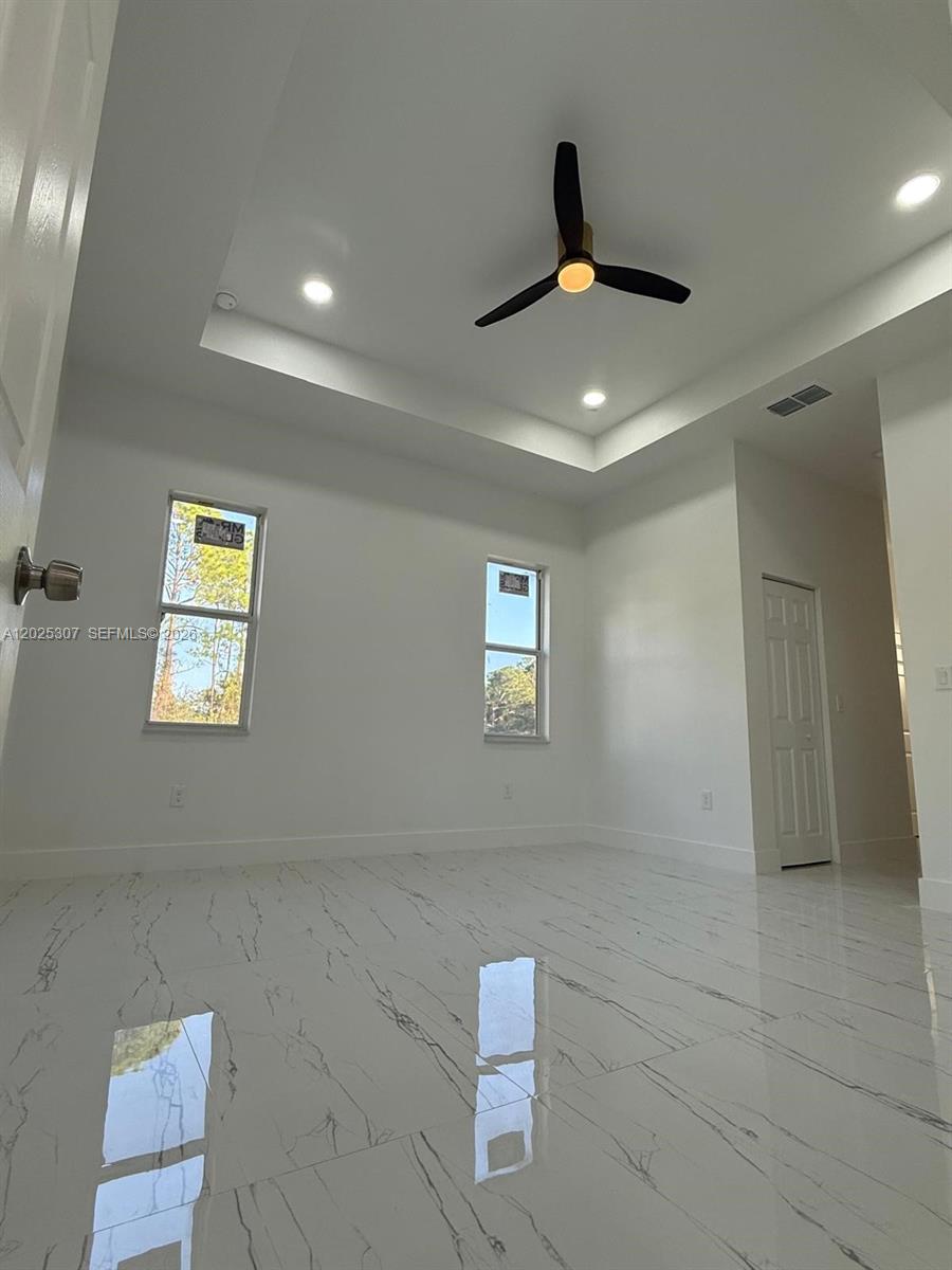 A bright room features white walls, a tray ceiling with a fan, and marble-look flooring — 4007 E 13 ST, Lehigh Acres FL 33972, LEHIGH ACRES, FL