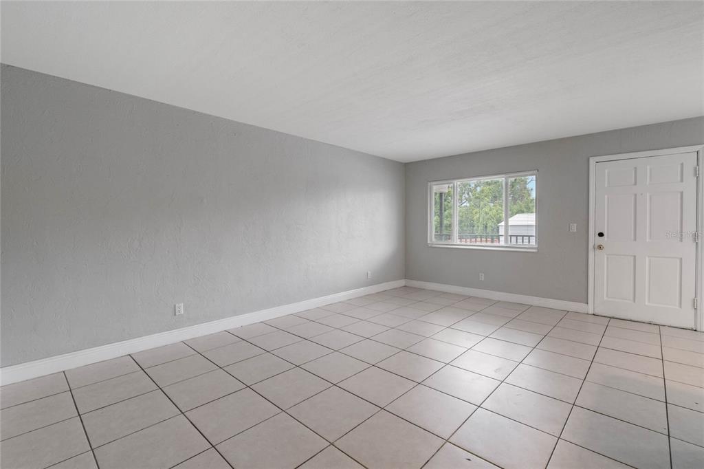 An empty room with gray walls, light-colored tile flooring, a window, and a white door — 900 S PENINSULA DRIVE UNIT 207, DAYTONA BEACH, FL