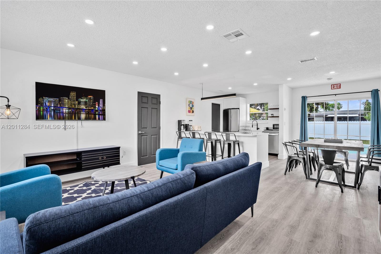An open-concept living and dining area features light wood flooring, blue furniture, and a kitchen — 7471 Hope St, Hollywood FL 33024, HOLLYWOOD, FL