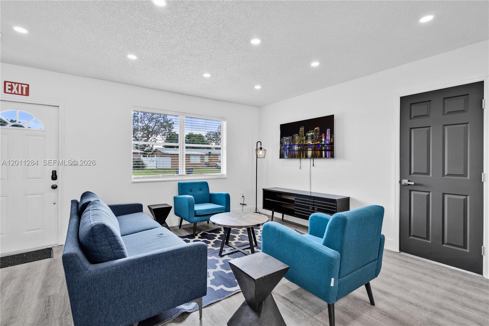 A living room features a blue sofa, two matching armchairs, a television, and light flooring — 7471 Hope St, Hollywood FL 33024, HOLLYWOOD, FL