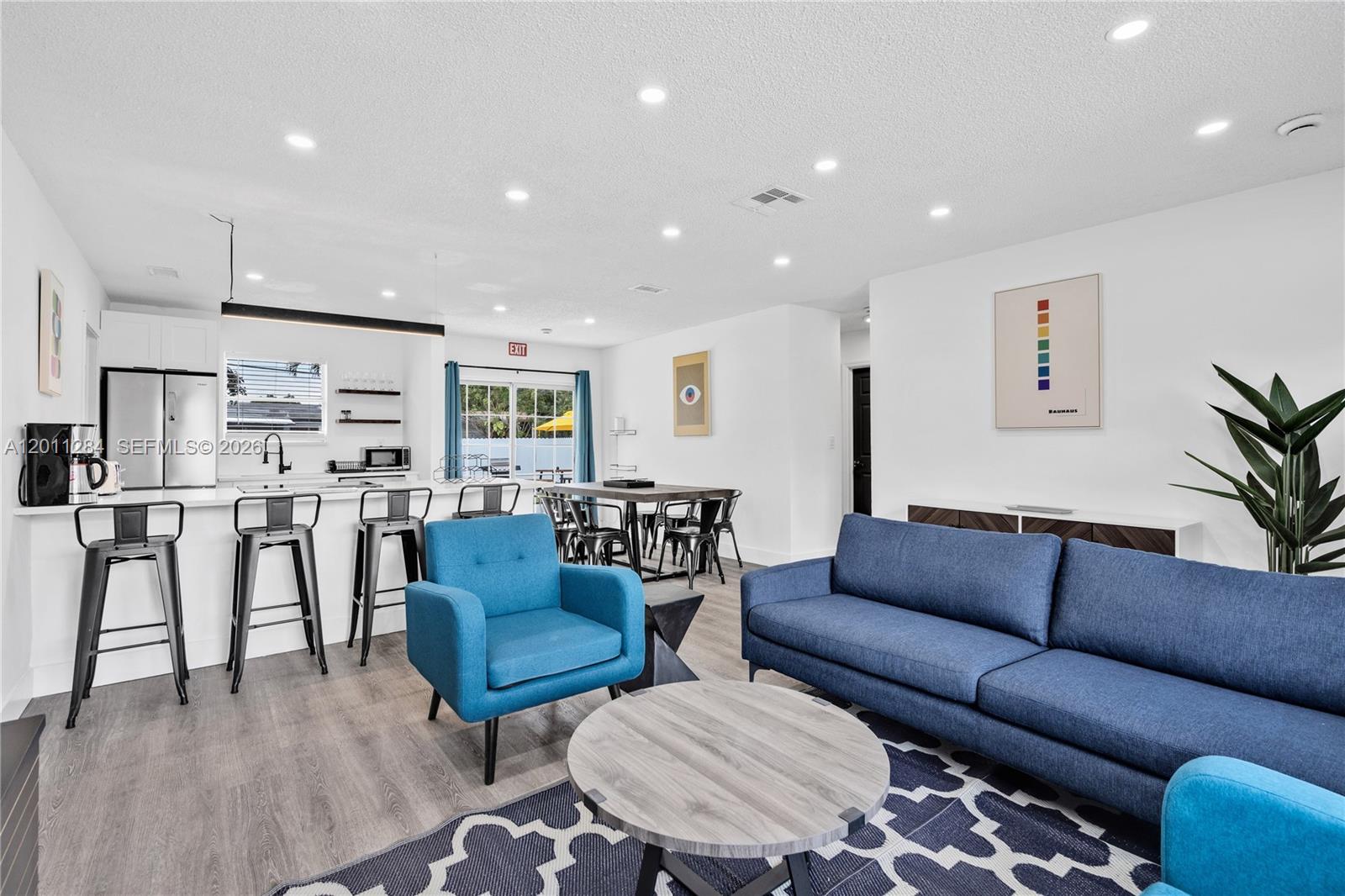 A modern open-concept living room and kitchen area with blue furniture and gray flooring — 7471 Hope St, Hollywood FL 33024, HOLLYWOOD, FL