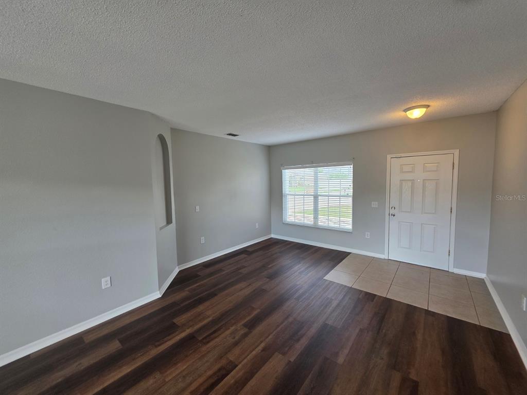An empty living room features gray walls, dark wood-look flooring, and a tiled entryway — 579 KILIMANJARO DRIVE, KISSIMMEE, FL