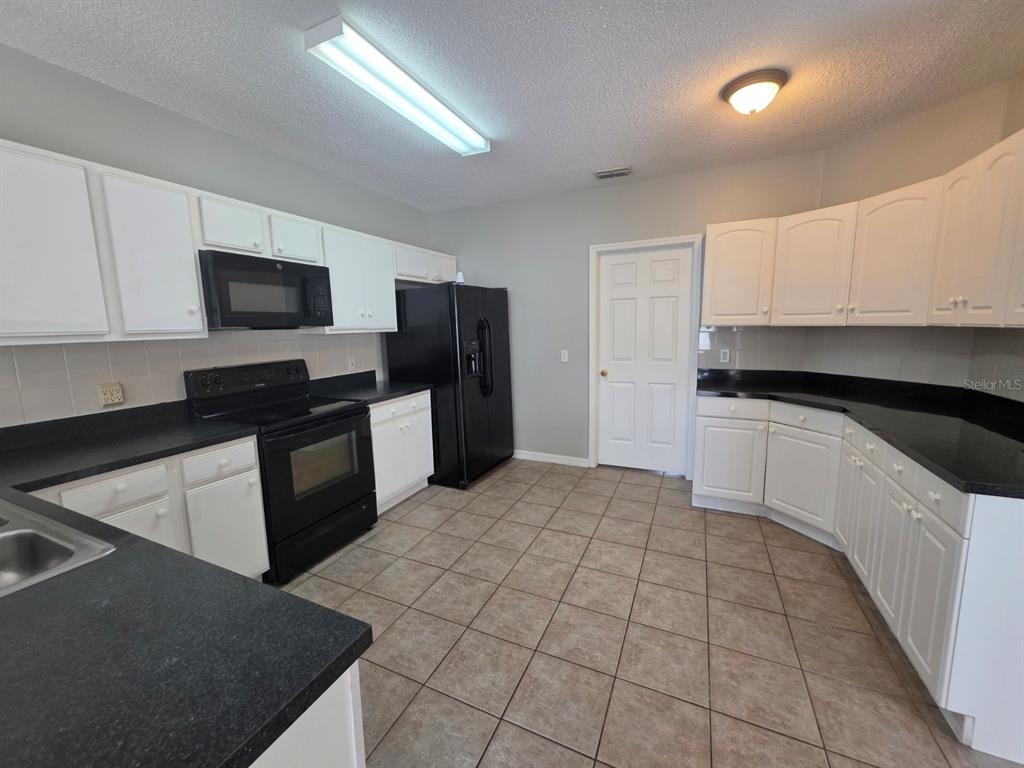 A kitchen features white cabinets, black countertops, black appliances, and light-colored tile flooring — 579 KILIMANJARO DRIVE, KISSIMMEE, FL